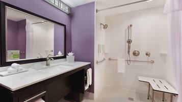 A modern bathroom with a large mirror, a sink, a shower with a handheld showerhead, and a vanity with a towel rack.