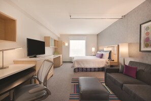 A modern hotel room with a bed, desk, chair, television, and a couch.