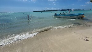 Una spiaggia con acque turchesi cristalline, una riva sabbiosa e una barca chiamata 'NAVEGANTE V' ancorata vicino alla battigia.