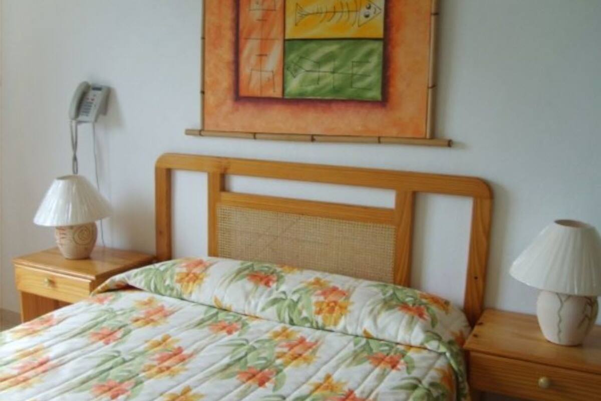 A bedroom with a wooden headboard, a floral bedspread, two bedside lamps, and a painting above the bed.