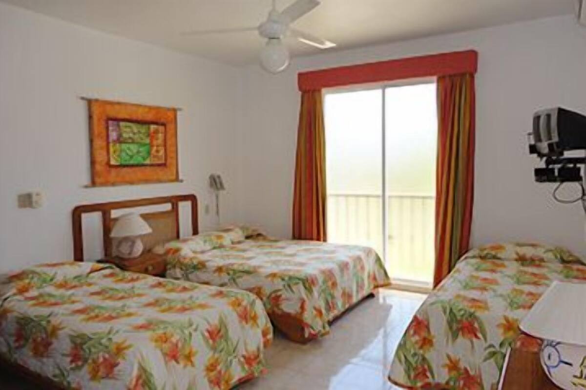 A room with two beds, a ceiling fan, a TV, and a balcony with curtains.