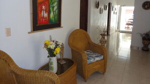 Un corridoio con poltrone in vimini, un vaso con fiori e un quadro colorato appeso al muro.