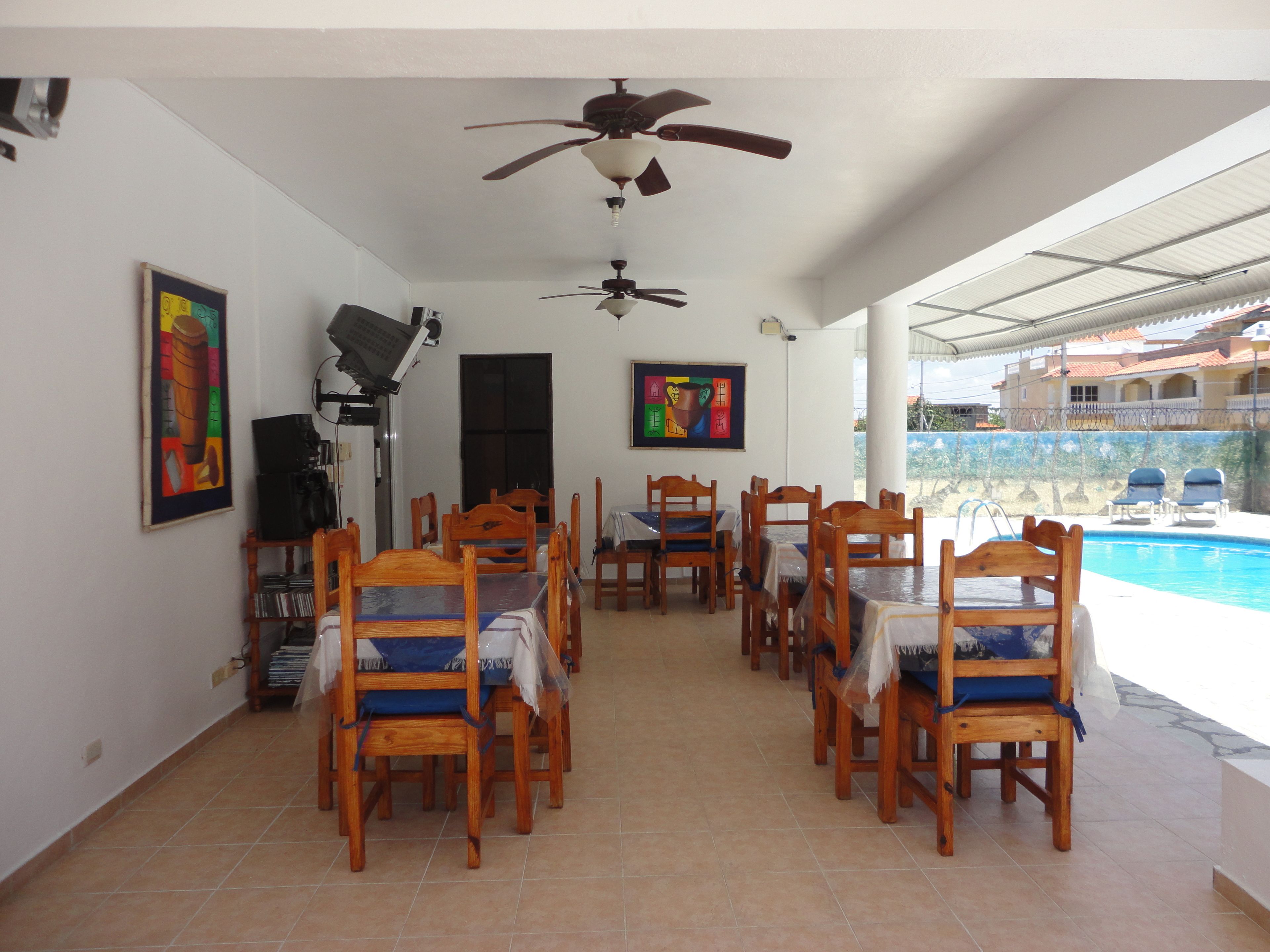 A dining area with wooden chairs and tables, ceiling fans, and a view of a swimming pool.