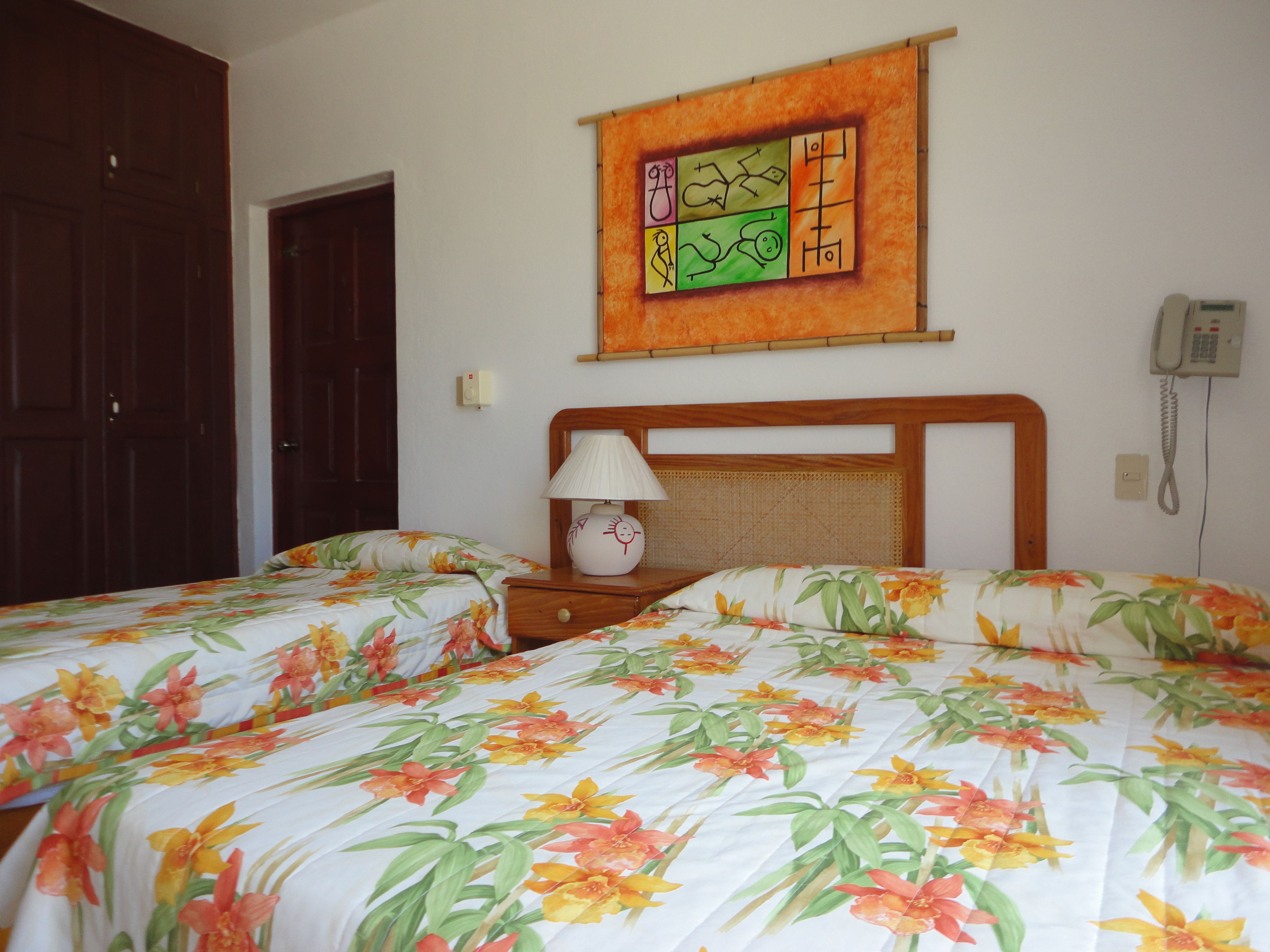 A bedroom with two beds, a nightstand, a lamp, a wall-mounted phone, and a door.