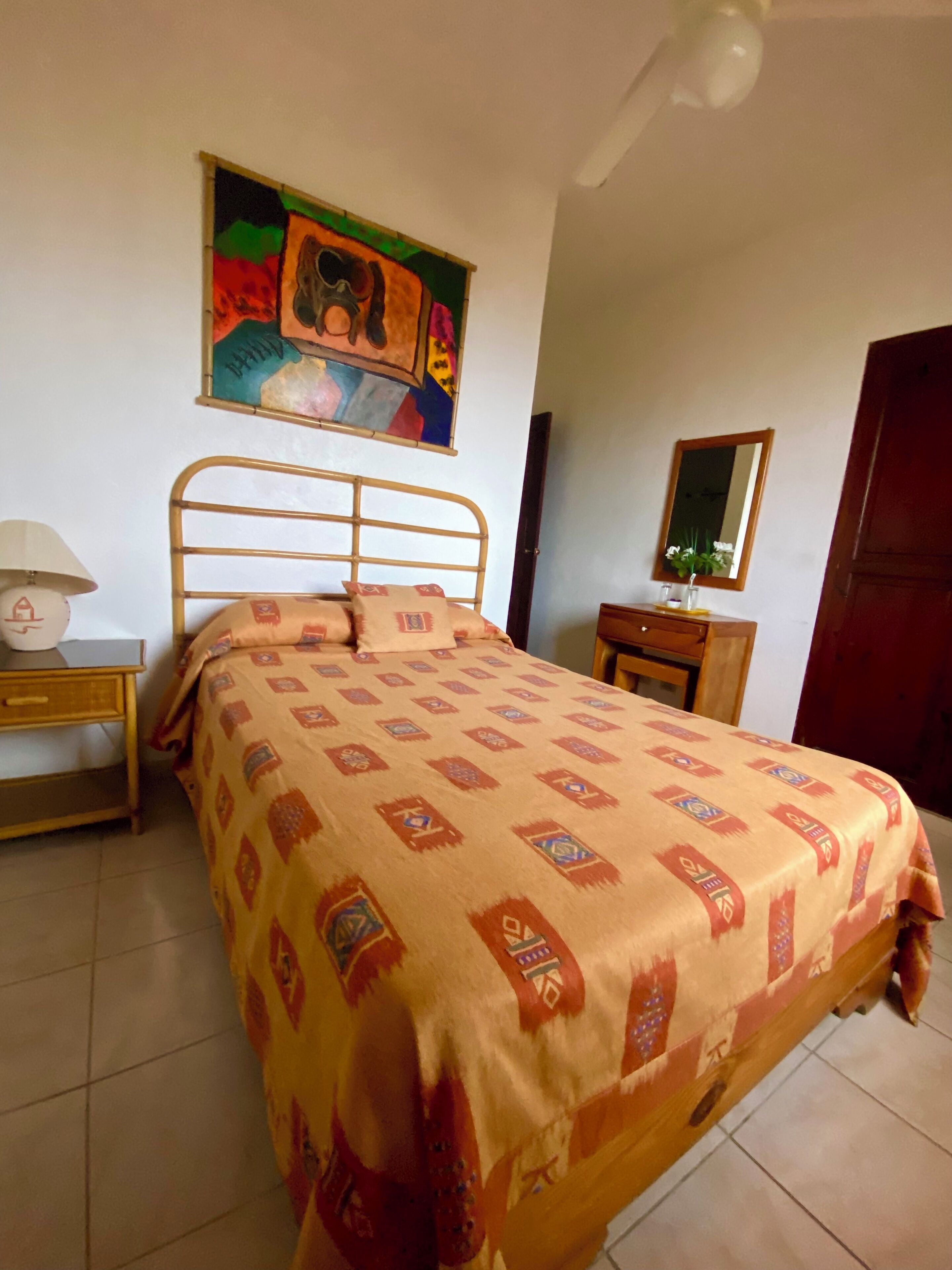 A bedroom with a bed, a nightstand, a bedside table, a mirror, and a painting on the wall.