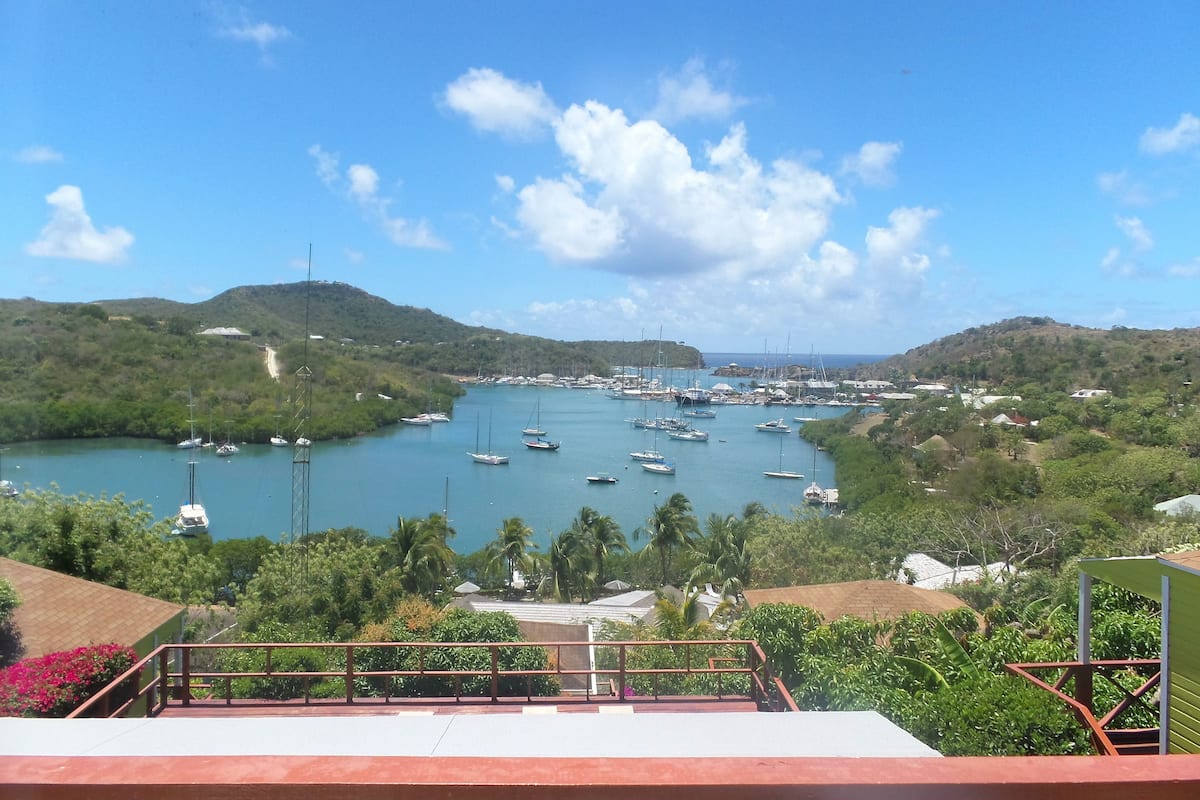 A coastal view with boats docked in a marina, surrounded by hills and greenery.