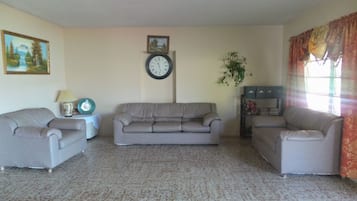 A living room with a beige sofa, a clock on the wall, and a plant.