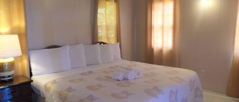 Una habitación de hotel con cama, mesita de noche, aire acondicionado y cortinas.