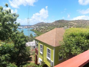 A green building with a tiled roof, surrounded by lush greenery and overlooking a harbor with boats.