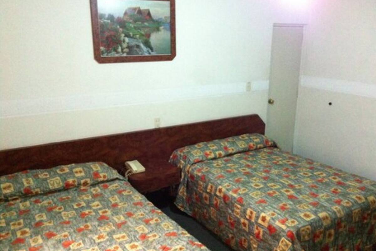 Una habitación de hotel con dos camas individuales, una mesita de noche pequeña con un teléfono y un cuadro enmarcado en la pared.
