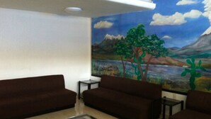 Una habitación con un mural de un paisaje, dos sofás marrones, una mesita y una mesa de centro de vidrio.