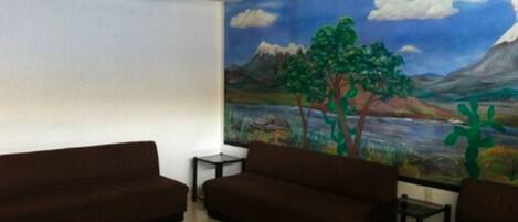 A room with a mural of a landscape, two brown sofas, a small table, and a glass coffee table.