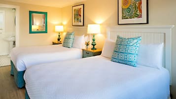Habitación de hotel con dos camas, cada una con almohada a juego, una mesita de noche con lámpara y un cuadro enmarcado en la pared.