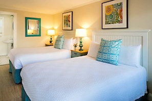A hotel room with two beds, each with a matching pillow, a nightstand with a lamp, and a framed picture on the wall. - Madison Inn (Oak Bluffs)