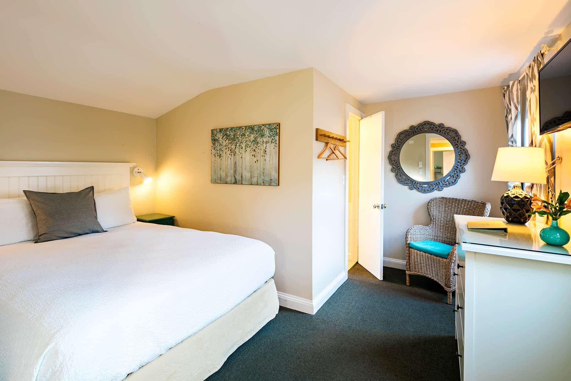 Ein Hotelzimmer mit einem Bett, einem Sessel, einem Schminktisch, einem Spiegel und einem Bild an der Wand.