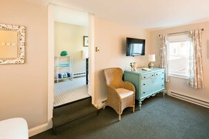 Habitación de hotel con una silla de mimbre, un aparador azul verdoso, un televisor de pantalla plana y vista de la calle a través de una ventana con cortinas.