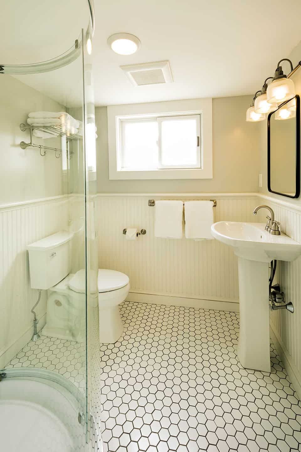 Une salle de bain avec une douche à parois de verre, des toilettes, un lavabo et une fenêtre située au-dessus du miroir.