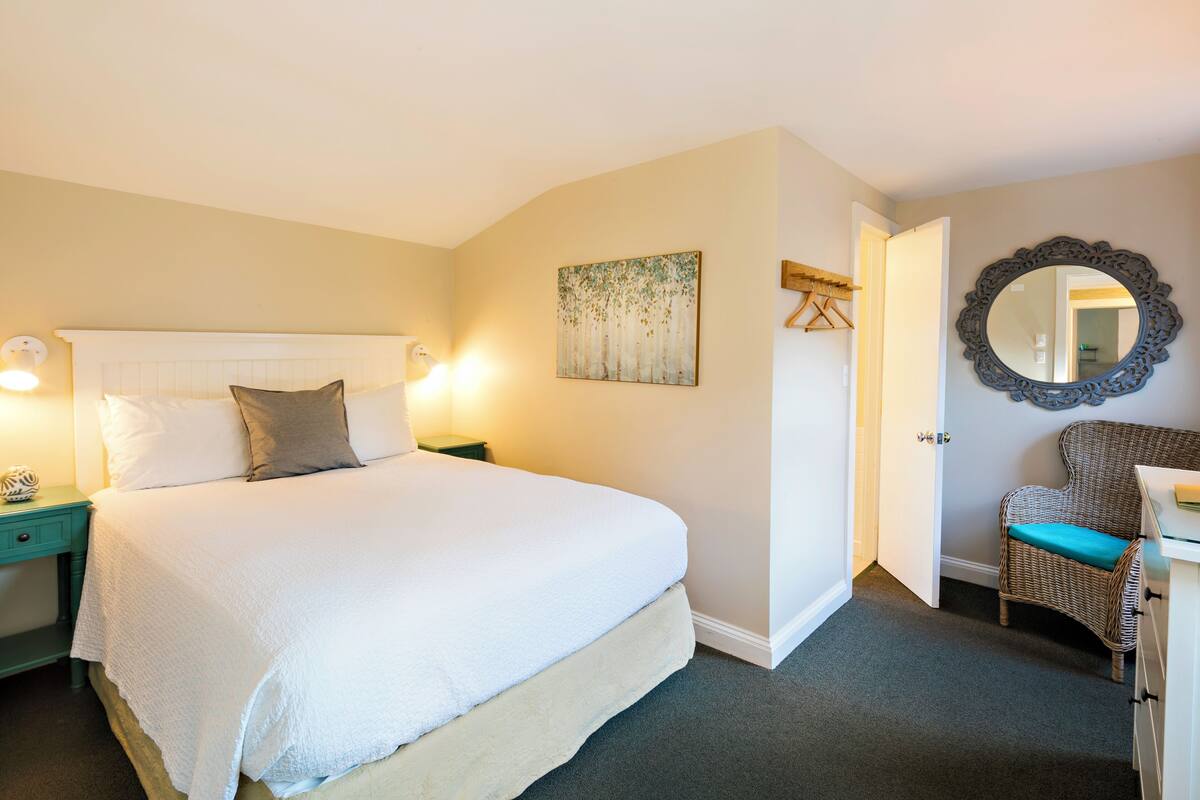 A bedroom with a bed, bedside tables, a chair, a mirror, and a door.