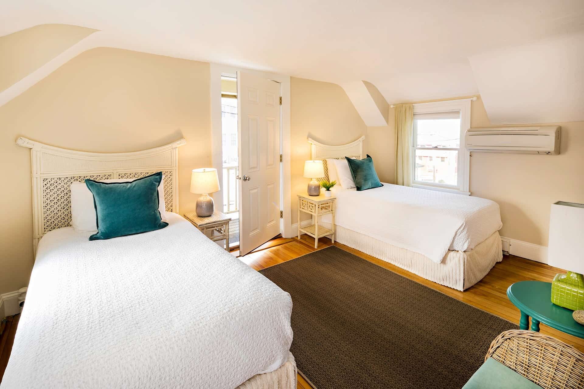 A hotel room with two beds, a small table, a chair, and a window with an air conditioner.