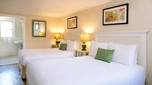 A hotel room with two beds, a bathroom, and a small table with lamps. - Madison Inn (Oak Bluffs)
