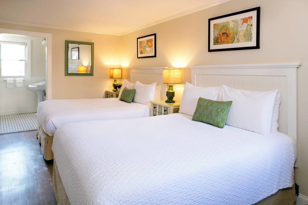 A hotel room with two beds, a bathroom, and a small table with lamps.