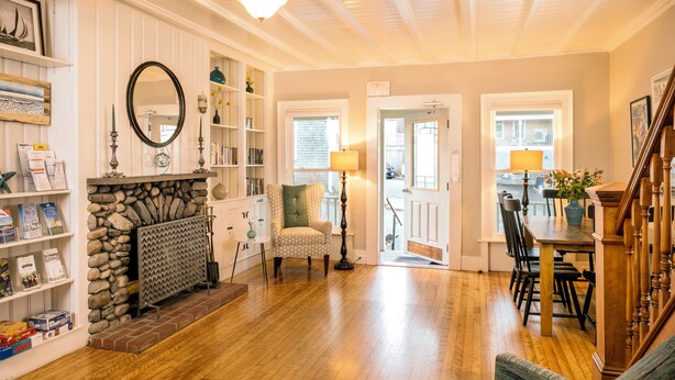 A cozy living room with a fireplace, bookshelves, a dining area, and a staircase. - Madison Inn (Oak Bluffs)