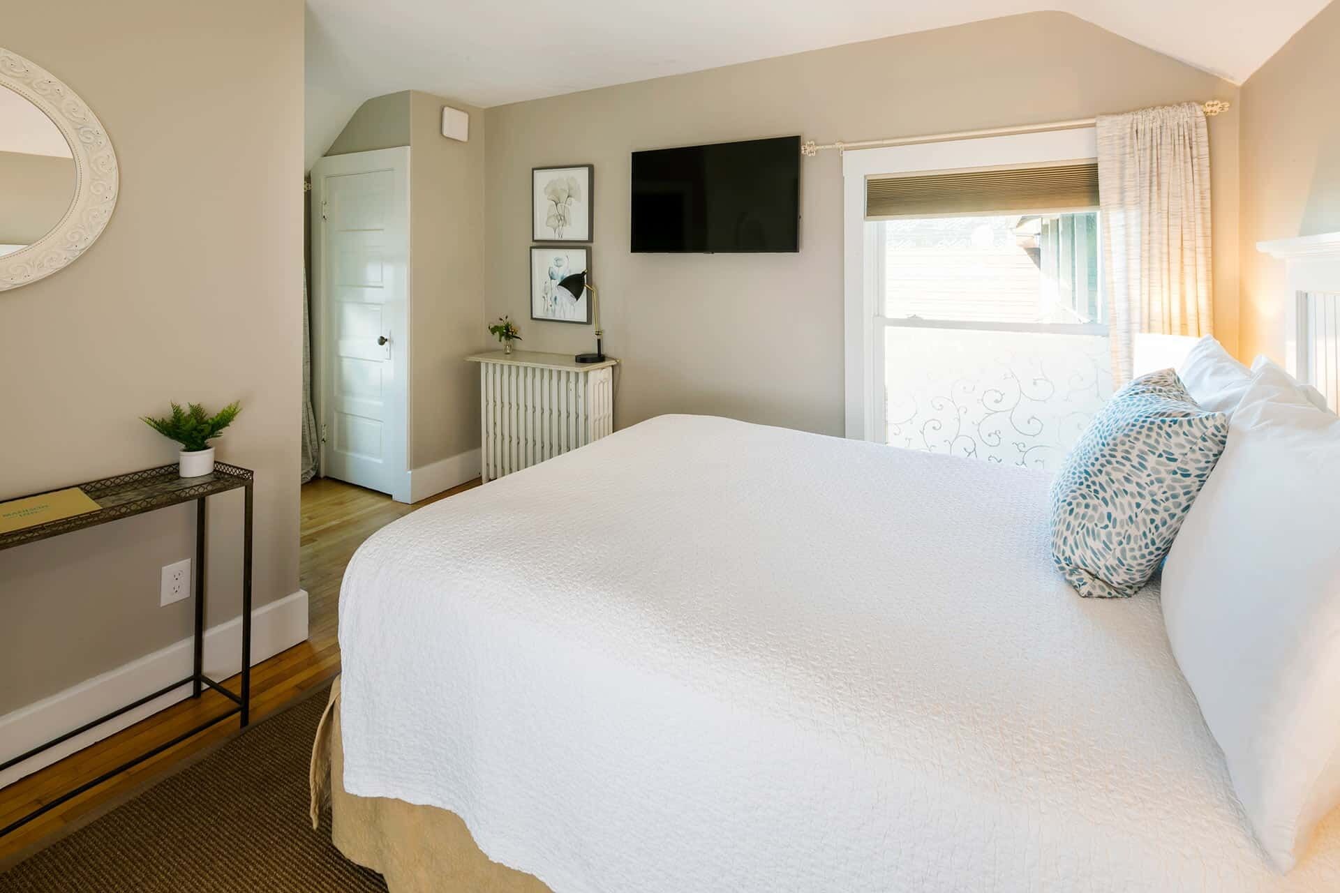 A bedroom with a large bed, a television mounted on the wall, a radiator, and a window with curtains.