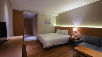 A hotel room with a bed, a sofa, a TV, a bedside table, and a lamp.