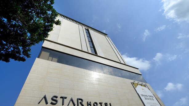 Exterior del HOTEL ASTAR, con cielo despejado y un cartel anunciando la GRAN INAUGURACIÓN en 2014.