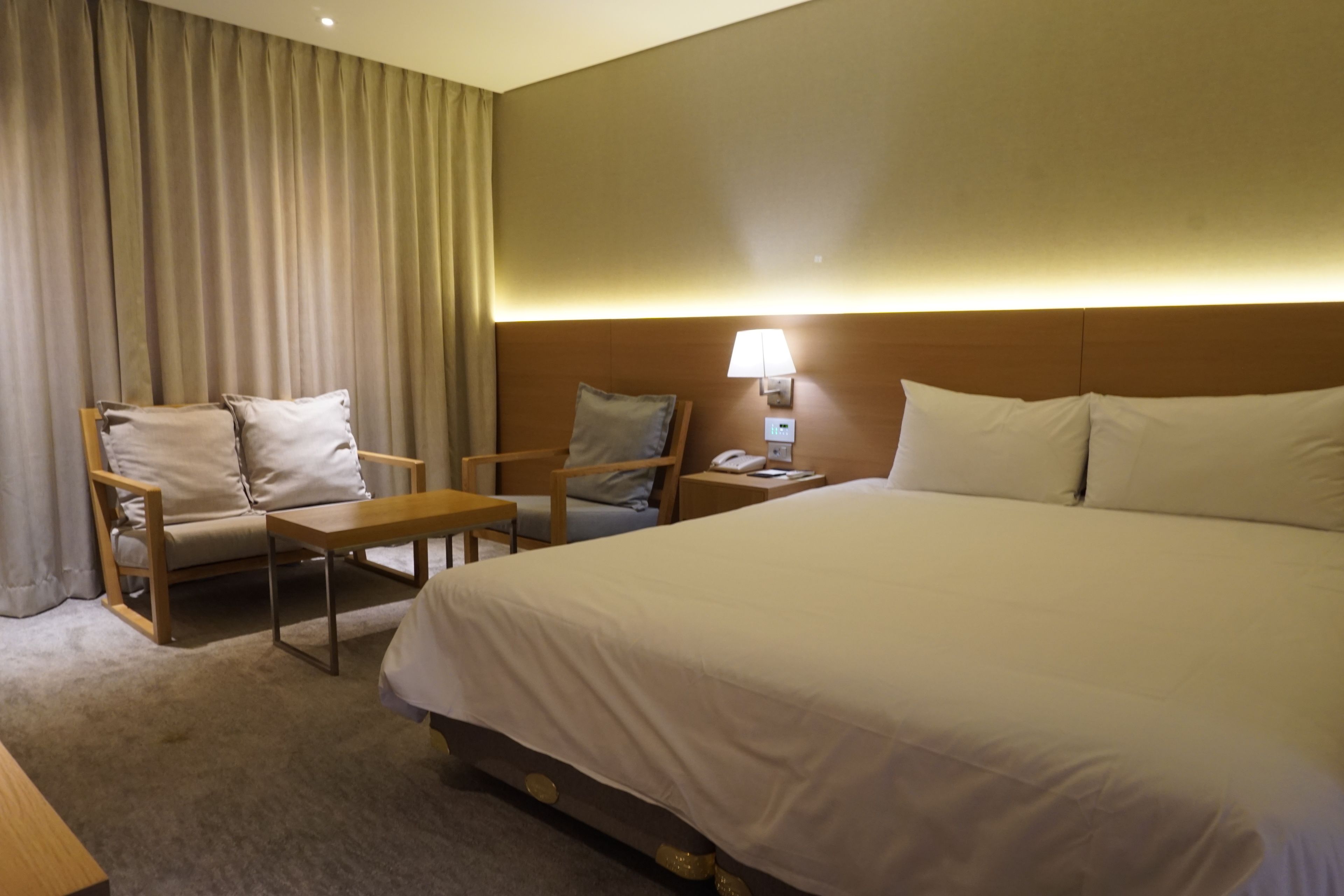 A hotel room with a large bed, two armchairs, a small table, a lamp, and a telephone.