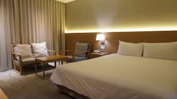 A hotel room with a large bed, two armchairs, a small table, a lamp, and a telephone.