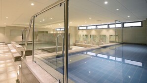 Una piscina interior con paredes de vidrio transparente, suelo de baldosas y diseño moderno.