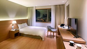 Una habitación de hotel con cama, escritorio, silla, televisión y ventana con cortinas.