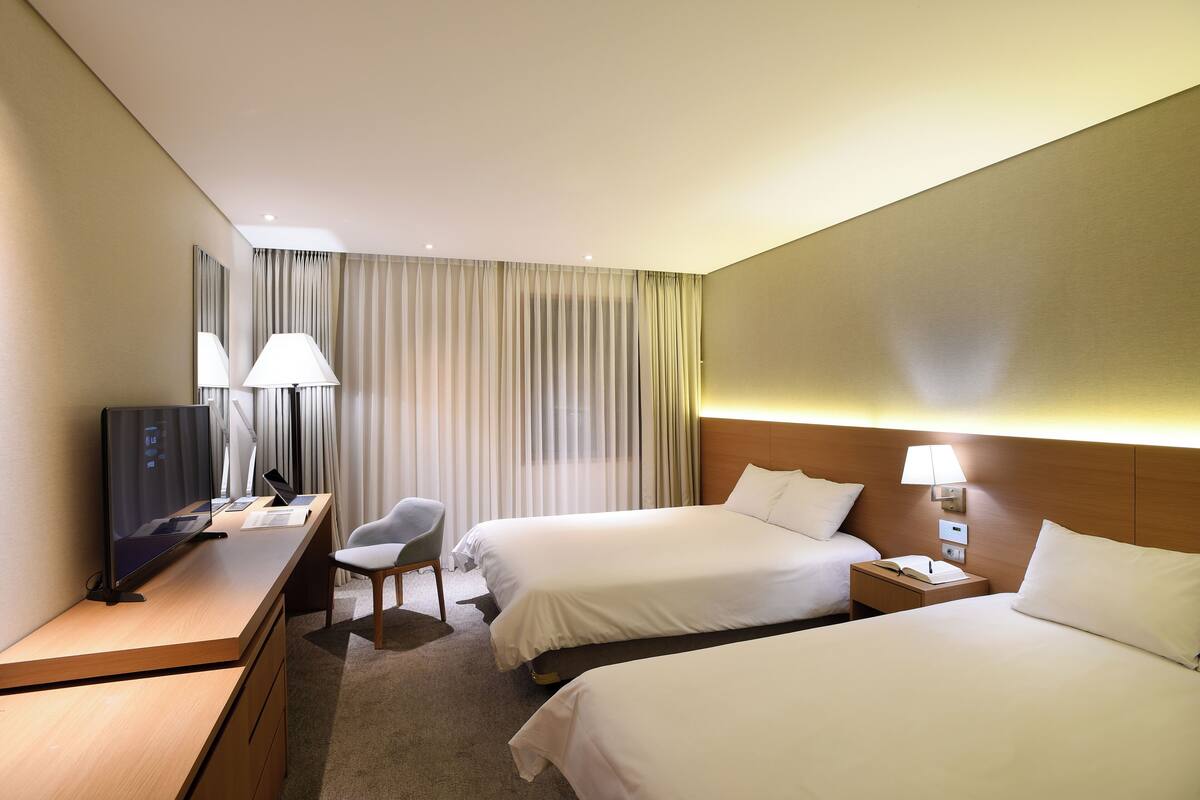 Habitación de hotel con dos camas, un escritorio con computadora, una silla, un televisor y una lámpara.