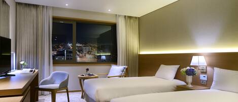 A hotel room with two beds, a desk, a chair, a TV, and a window with a city view.