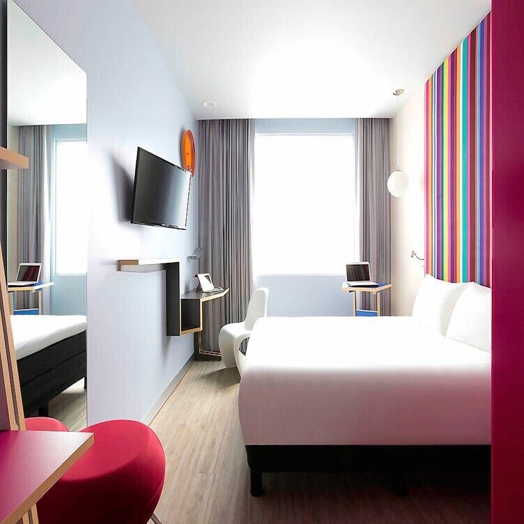 Una habitación de hotel moderna con una cama grande, un escritorio, una silla, un televisor y una ventana con cortinas.