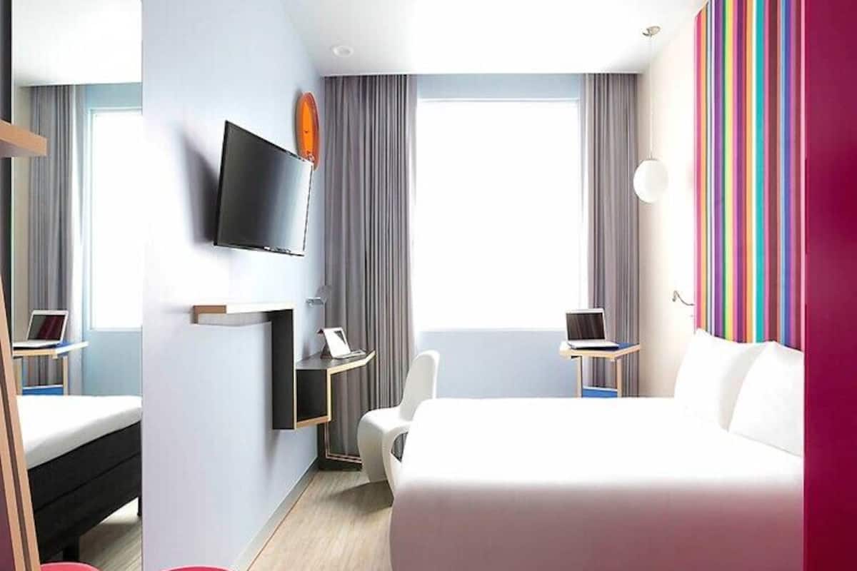Ett modernt hotellrum med en stor sÀng, ett skrivbord, en stol, en TV och ett fönster med gardiner.
