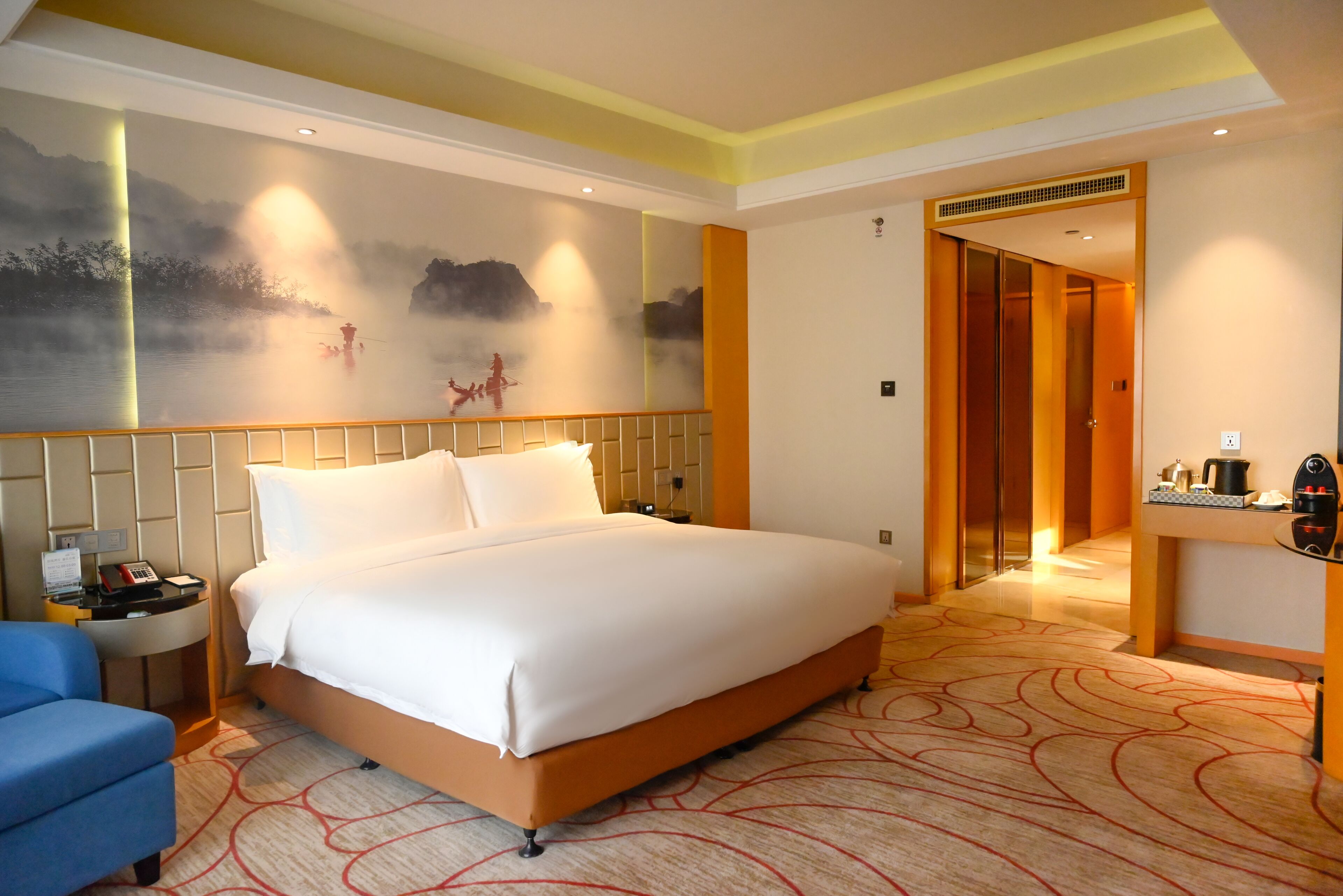 A hotel room with a large bed, a desk, a chair, and a wall mural.