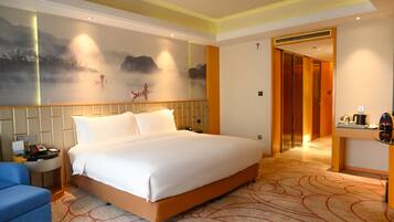 A hotel room with a large bed, a desk, a chair, and a wall mural.