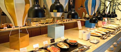 A buffet with various food items, serving utensils, and hanging lamps.