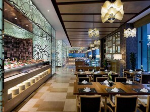 A restaurant with a buffet on the left, wooden tables with white napkins, and modern pendant lighting. - Pullman Wenzhou (Wenzhou)