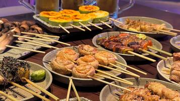 A variety of skewered meats and vegetables on ceramic plates, with beer mugs in the background.