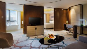 A hotel room with a large bed, a TV, a desk, a chair, a small table with fruit, and a view of the city through a window. - Pullman Wenzhou (Wenzhou)