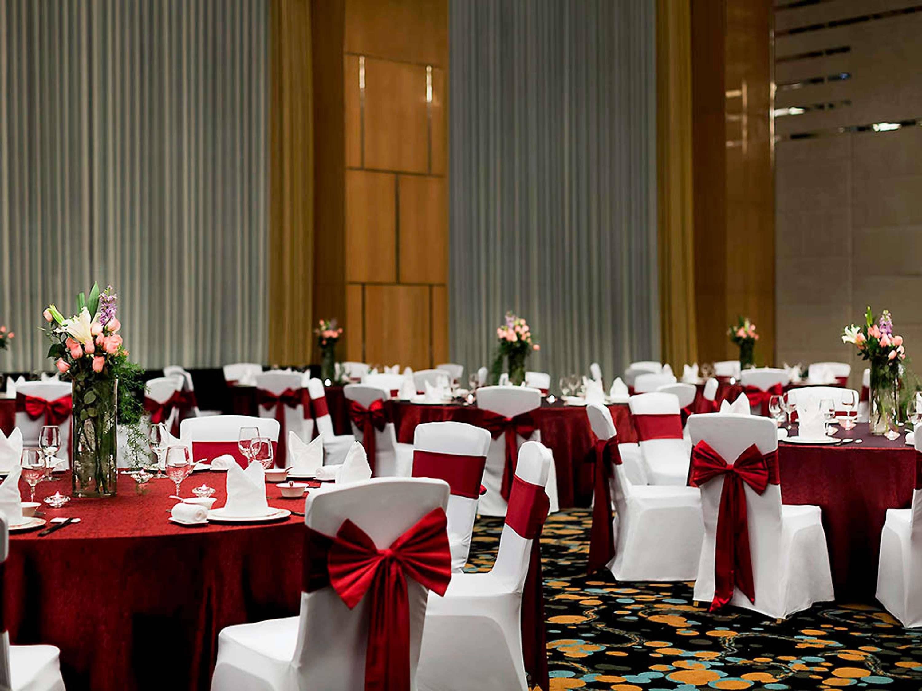 A banquet hall with round tables, white chairs with red sashes, and floral centerpieces.