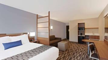 A hotel room with a bed, a desk, a chair, a small table, a sofa, a ladder, and a kitchenette.