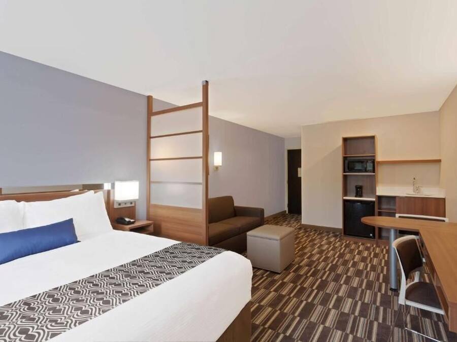 A hotel room with a bed, a desk, a chair, a small table, a sofa, a ladder, and a kitchenette.