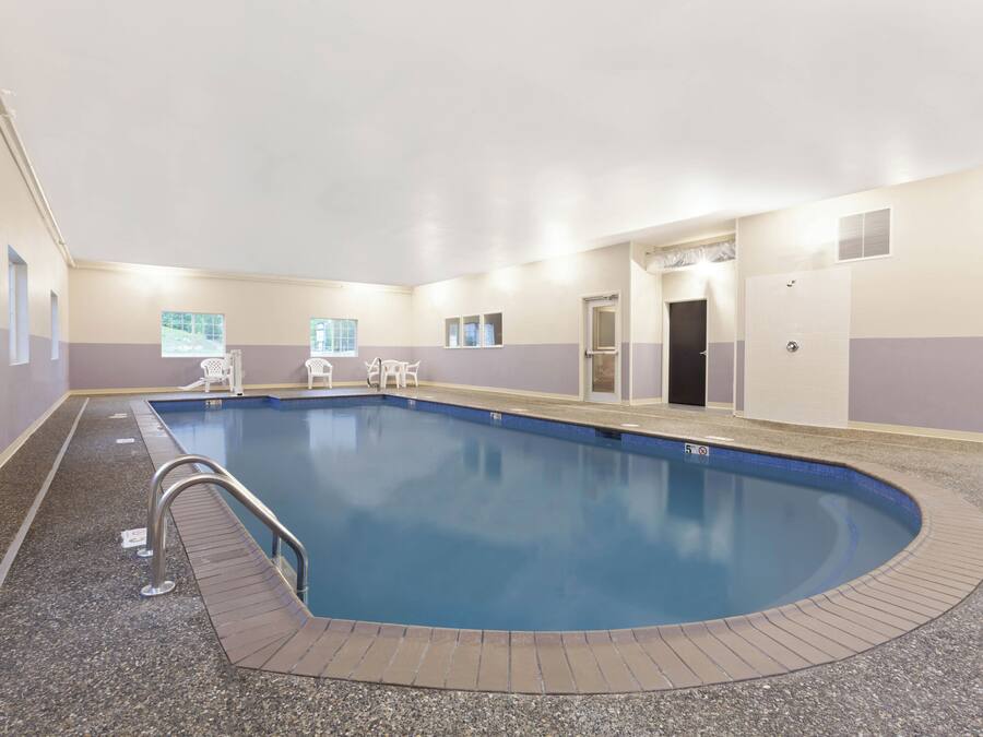 An indoor swimming pool with a tiled edge, a metal handrail, and a door leading to another room.