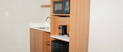 Una kitchenette compacta con microondas, cafetera y un refrigerador pequeño.