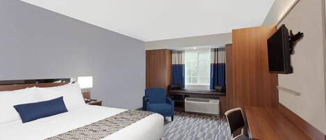 A hotel room with a large bed, a desk, a chair, a TV mounted on the wall, and a window with curtains.