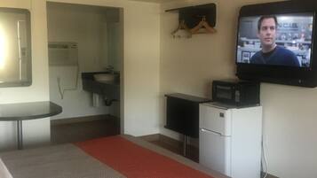 A hotel room with a bed, a small kitchenette, a TV mounted on the wall, and a bathroom visible through an open door.